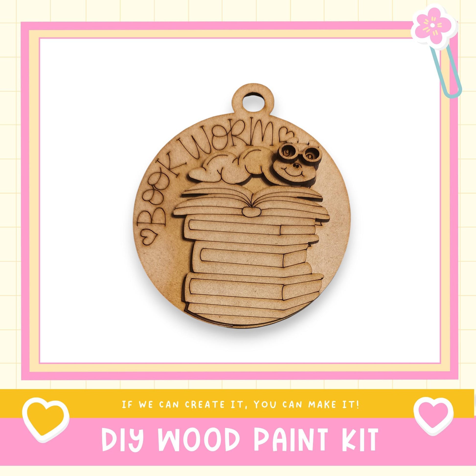 a wooden pendant with a design of stacked books and a smiling character, along with text that says "Book Worm" and "DIY WOOD PAINT KIT".