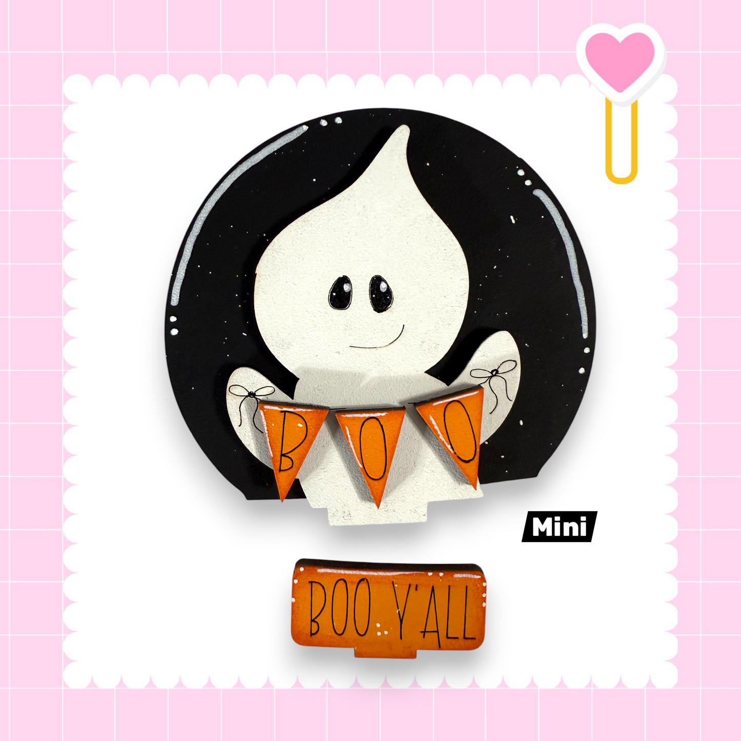 a Halloween-themed decoration with a ghost holding orange banners that say "BOO Y'ALL". The decoration is set against a pink background with a scalloped edge.