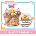 a DIY wood paint kit for creating a wooden basket with a duck and Christmas decorations. The basket is filled with ornaments and a small wooden sign that says "Welcome".