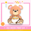 A wooden teddy bear wearing a diaper and holding a spoon, with a pink and white striped border and a star decoration.