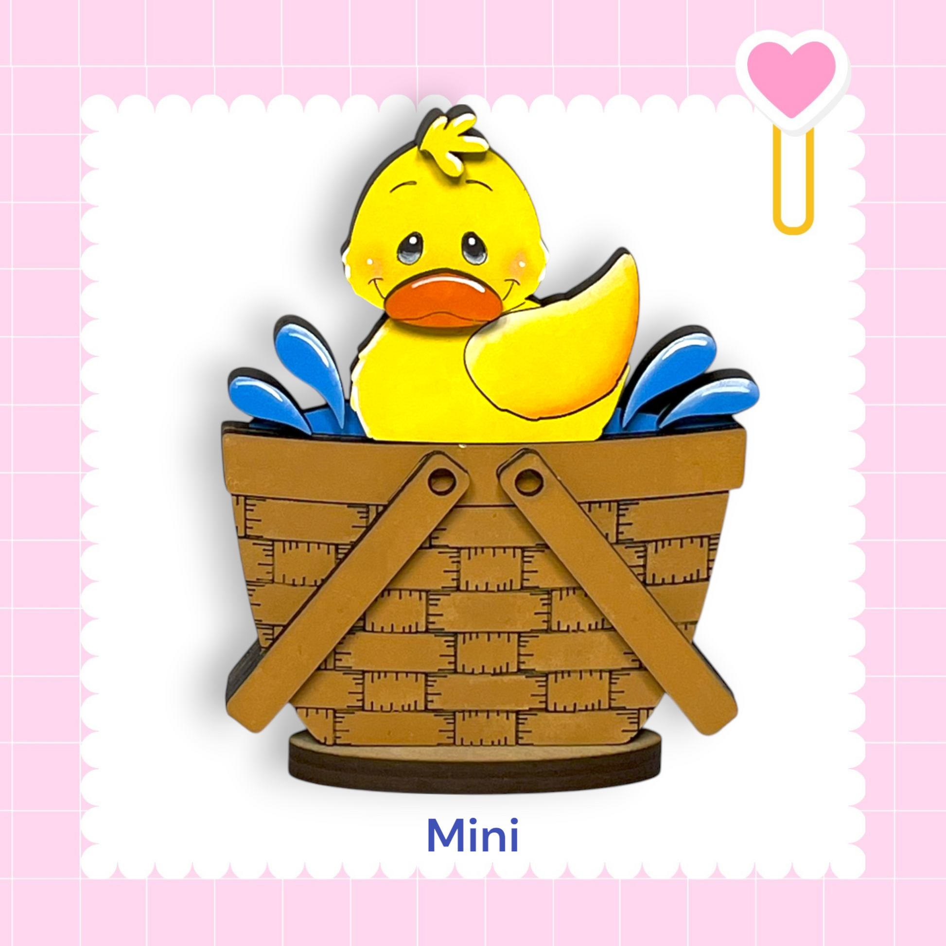 A yellow duck sitting in a brown basket, with a pink heart and a heart-shaped object to the right.