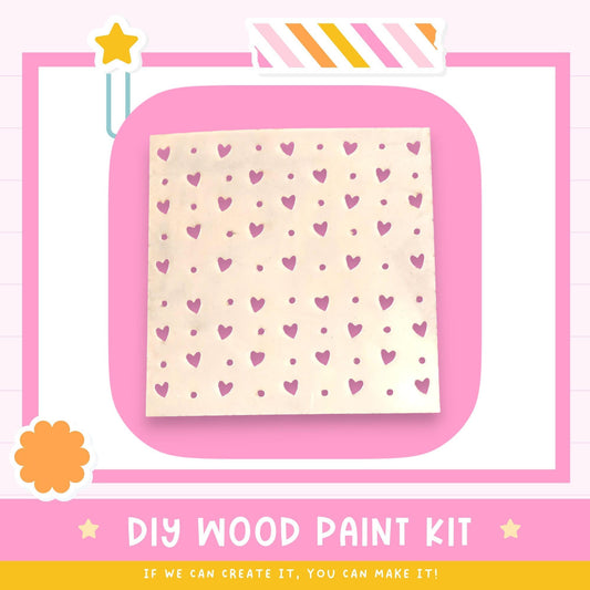 The image is a promotional poster for a DIY wood paint kit. It features a heart-shaped stencil with a pattern of pink hearts on a white background, along with a star and a flower. The text on the poster encourages viewers to "If we can create it, you can make it!"