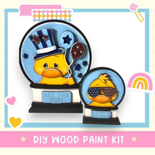 a DIY wood paint kit for creating a wooden snow globe with a duck and American flags. The kit includes a wooden base and a blue snow globe with a duck wearing a top hat and holding a star and a balloon. The kit is designed for creating a decorative snow globe with a playful and patriotic theme.