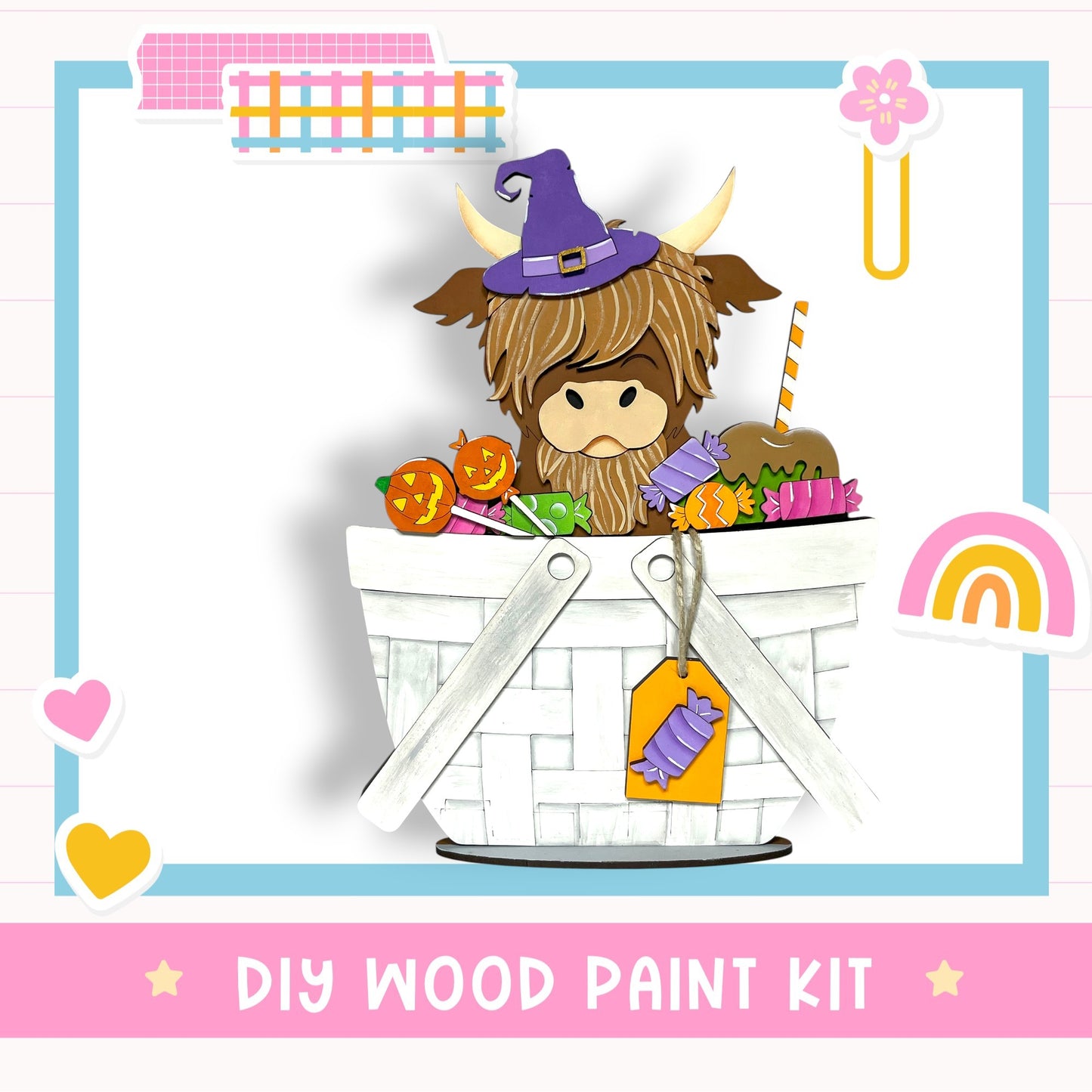 A whimsical illustration of a cow wearing a witch's hat and sitting in a basket filled with Halloween-themed items, such as pumpkins and candy apples. The image is framed by a pink border and includes various decorative elements like hearts and a rainbow. The text "DIY WOOD PAINT KIT" is displayed at the bottom of the image.