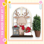 A wooden deer figurine wearing a red scarf and hat stands on a shelf next to a potted plant, with a lantern and star decoration nearby.
