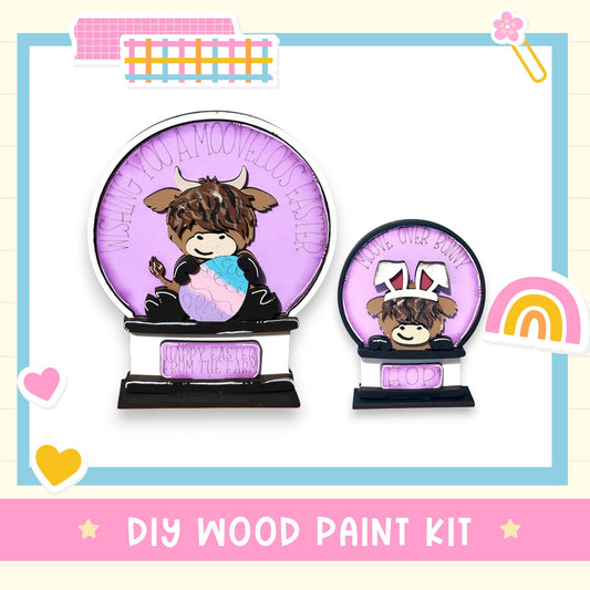 The image is a DIY wood paint kit featuring a wooden snow globe with a cow and a smaller snow globe with a bunny. The text "DIY WOOD PAINT KIT" is displayed at the bottom of the image.