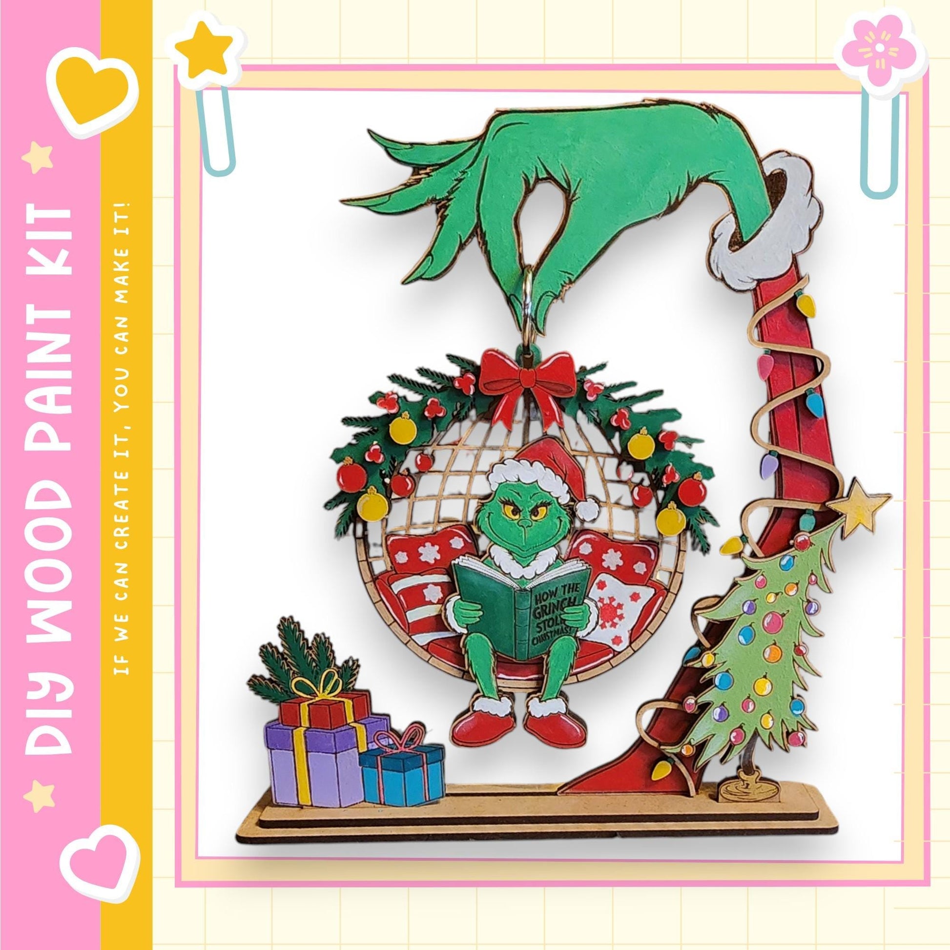A hand-painted Christmas ornament featuring a green Grinch-like character holding a book, surrounded by holiday decorations such as a wreath, presents, and a Christmas tree.