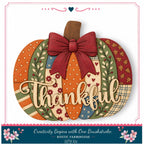 A hand-carved wooden pumpkin with a bow and the word "Thankful" written on it, surrounded by various autumn-themed decorations.