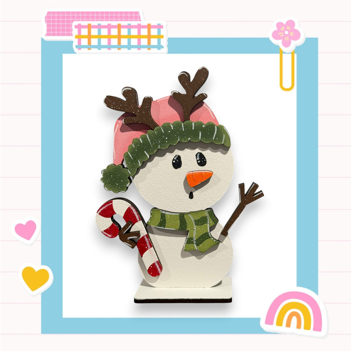 A snowman wearing a green hat and scarf, holding a red and white striped candy cane, is surrounded by various colorful and whimsical elements such as hearts, a rainbow, and a flower.