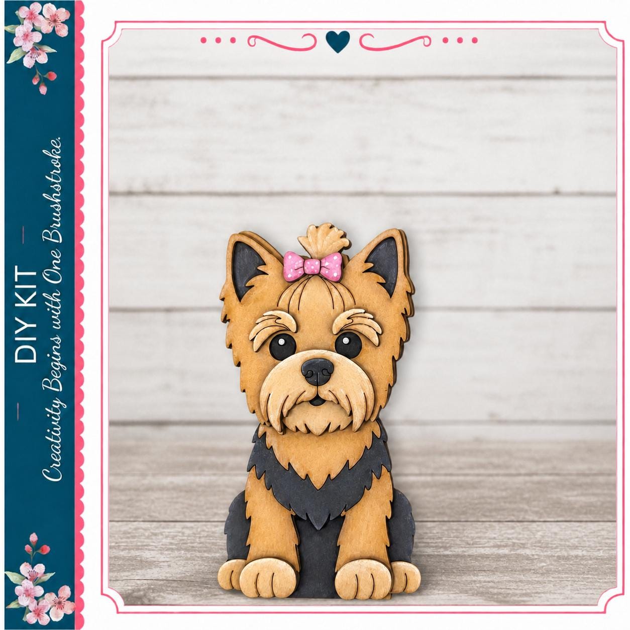 A wooden cutout of a Yorkshire Terrier dog with a pink bow on its head, sitting on a wooden surface against a white background.