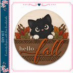 A wooden sign with a black cat peeking out from behind a decorative border, surrounded by autumn foliage. The sign has the text "Hello fall" written on it.