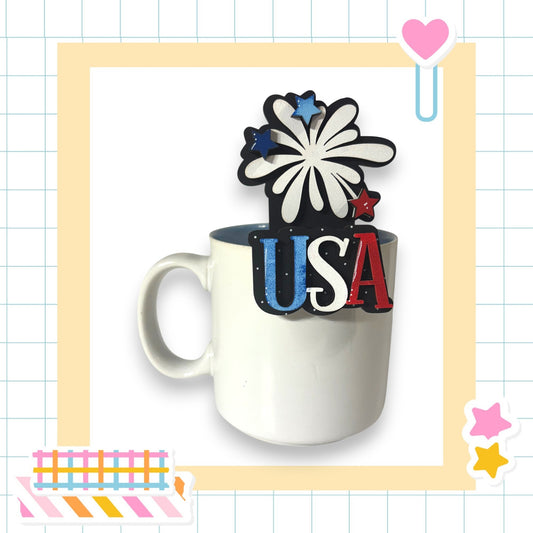 A white mug with the word "USA" written on it, surrounded by various colorful and decorative elements such as stars, hearts, and a rocket ship.