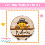 a wooden sign with a duck wearing a hat and the word "Welcome" written on it. The sign is surrounded by various decorative elements, including a pink banner, a heart, and a star.