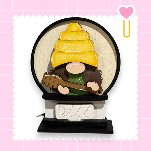 A gnome wearing a yellow hat and holding a guitar is depicted in the center of the image, set against a pink background with a heart shape and a small yellow heart shape.