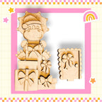 A wooden toy figure wearing a Santa hat and holding a gift box, surrounded by other wooden shapes and decorations, all set against a pink and yellow checkered background.