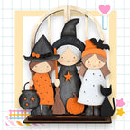 A Halloween-themed display featuring three cartoon-style girls dressed as witches, with a black cat and a pumpkin as part of the scene.