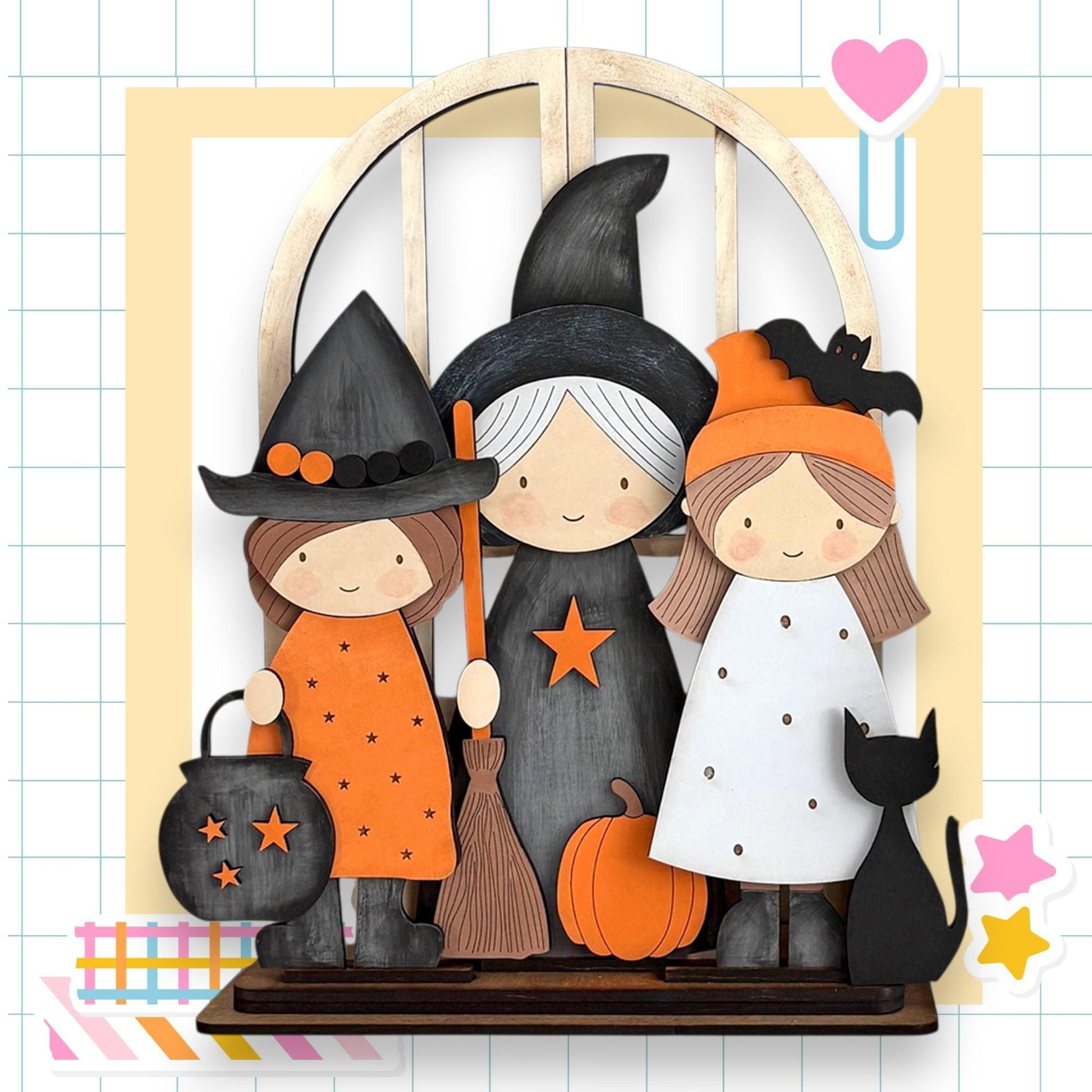 A Halloween-themed display featuring three cartoon-style girls dressed as witches, with a black cat and a pumpkin as part of the scene.