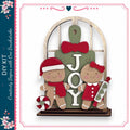 A DIY kit featuring a gingerbread man and a girl, with the word "JOY" displayed on a green sign.
