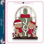 A DIY kit featuring a gingerbread man and a girl, with the word "JOY" displayed on a green sign.
