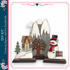 a snowman and a small house, both made of wood and decorated with various winter elements such as a scarf, hat, and carrot nose.