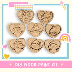 a DIY wood paint kit with heart-shaped ornaments, including a reindeer, a cat, a bird, a snowman, a Santa hat, a rainbow, and a smiling face.