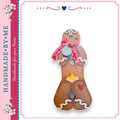 A handcrafted gingerbread man figure with a blue tag that says "Joy" and a red bow around its neck.