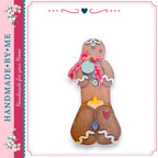 A handcrafted gingerbread man figure with a blue tag that says "Joy" and a red bow around its neck.