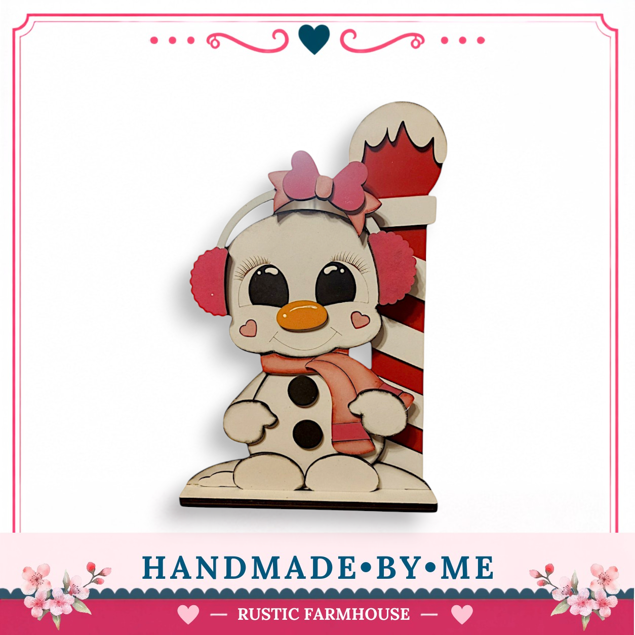A hand-made wooden snowman figure with a red and white striped pole, wearing a pink bow and earmuffs, sitting on a white base.