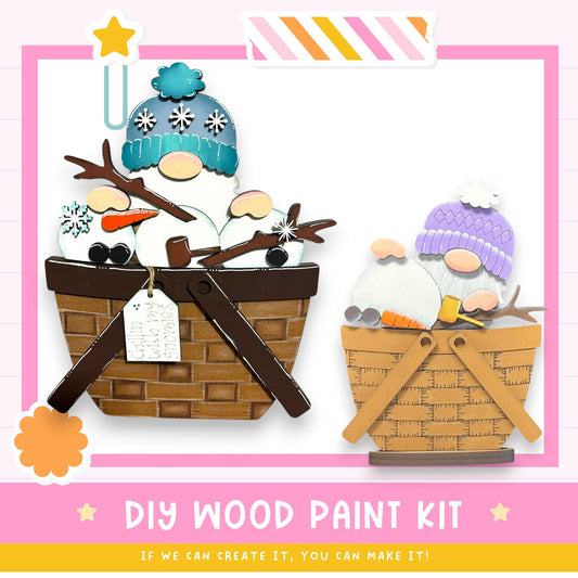 The image is a DIY wood paint kit featuring two wooden gnome-shaped figures in baskets, set against a pink and white background.