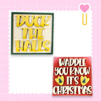 two signs with text on them, one in yellow and one in red, both with a heart symbol. The yellow sign says "Duck the Halls" and the red sign says "Waddle you know it's Christmas".