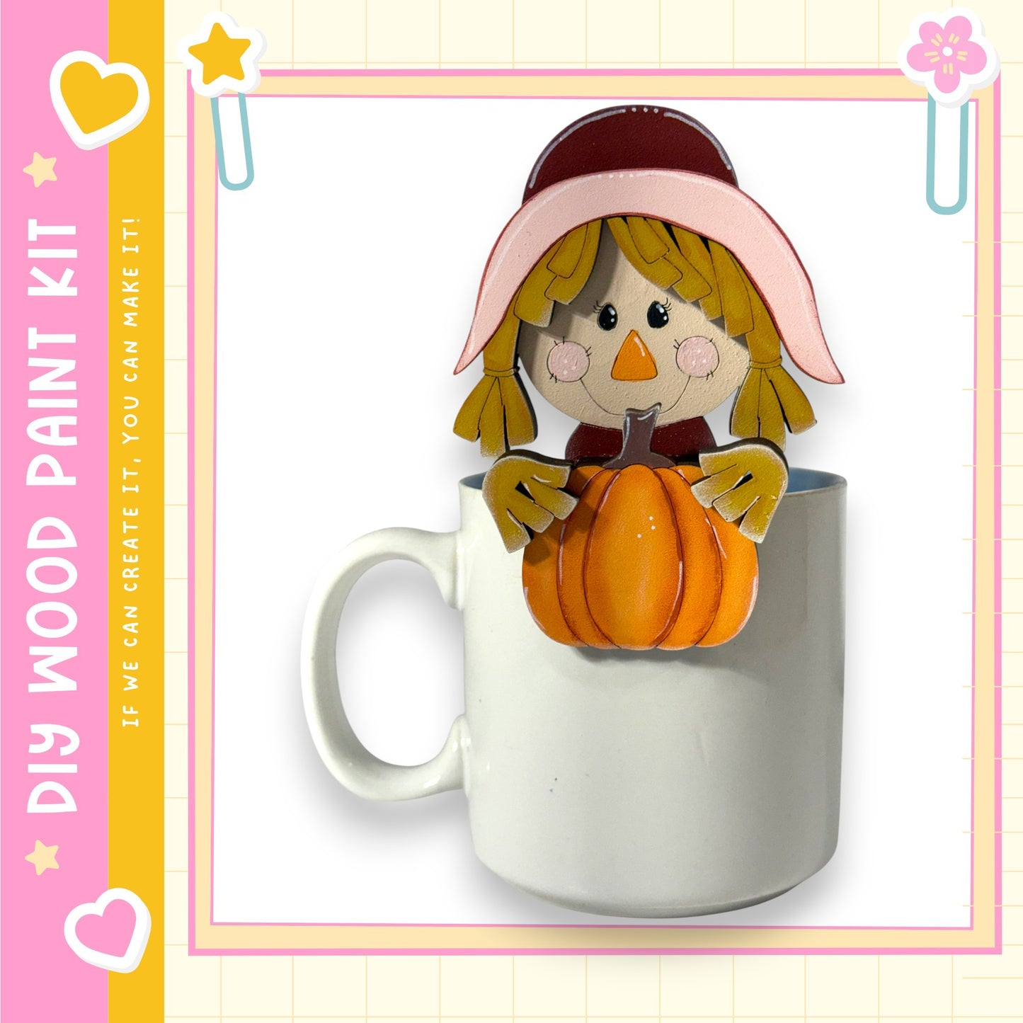 A white mug with a paper craft pumpkin and a paper craft scarecrow figure on it, set against a pink and yellow background.