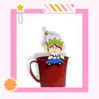 A cartoon elf figurine is sitting inside a red mug, with a toy car attached to the mug.