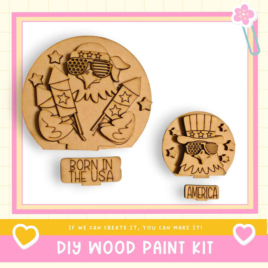 two wooden cutouts of American flags, one larger and one smaller, along with a sign that says "Born in the USA". The text below the cutouts reads "DIY WOOD PAINT KIT" and "If we can create it, you can make it!".
