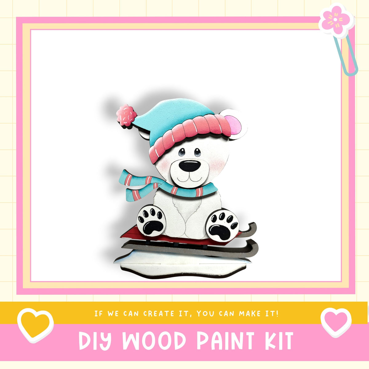 A wooden bear wearing a hat and scarf sits on a sled, with a DIY wood paint kit and a heart-shaped sticker on the bottom right corner.