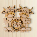 A wooden cutout of two smiling cows, one with a bow, is mounted on a wooden surface.