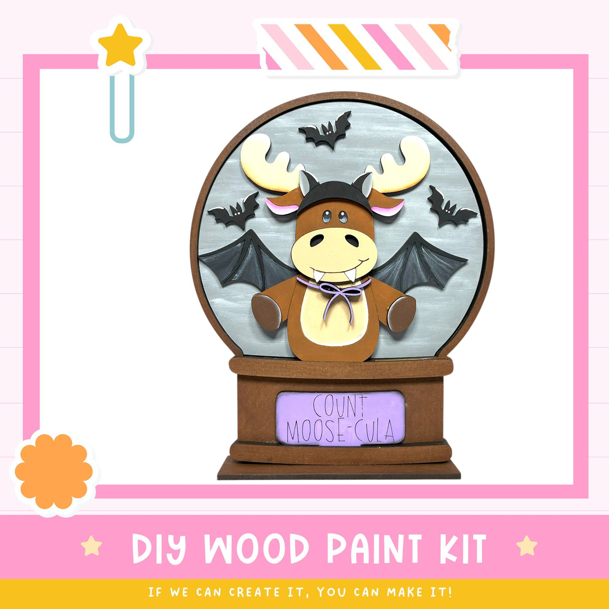 A wooden snow globe with a moose wearing a hat and holding bats, set against a pink and white background.