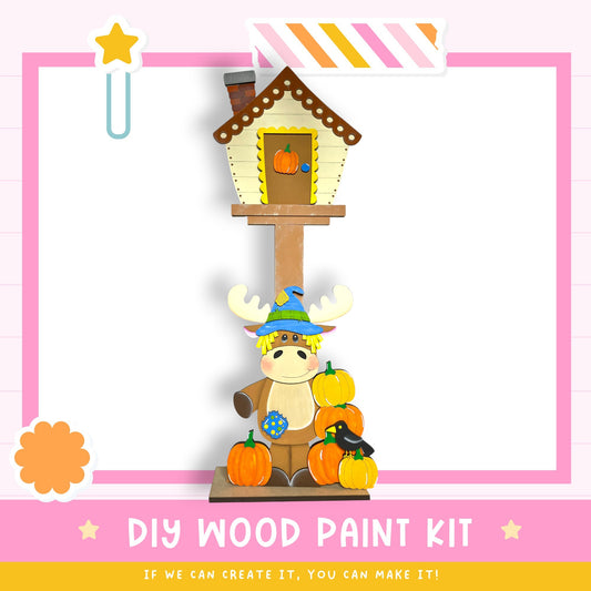 a DIY wood paint kit with a cartoon moose and pumpkins, along with a star decoration. The kit appears to be made of wood and is designed for painting.