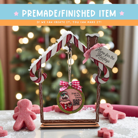 a festive scene with a candy cane-shaped ornament, a small gingerbread man, and a sign that reads "Home for the Holidays". The background is blurred, but it appears to be a Christmas tree, suggesting a holiday celebration.