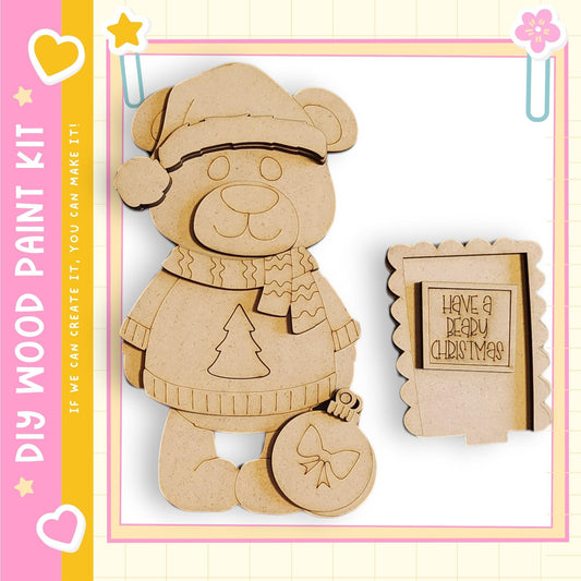 A wooden bear wearing a Santa hat and scarf, holding a Christmas ornament, and a small wooden frame with a message.