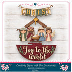 The image is a Christmas nativity scene with a wooden sign that says "Joy to the world" and a banner that says "CHRIST". The scene includes three figures representing the baby Jesus, Mary, and Joseph, along with a wooden hutch and a star. The background is a white wooden wall with a floral border.