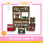 The image is a DIY wood paint kit featuring a wooden sign with a cowbells ring and a Christmas message, along with various other wooden decorations.