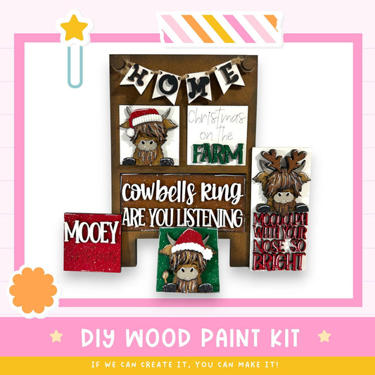 The image is a DIY wood paint kit featuring a wooden sign with a cowbells ring and a Christmas message, along with various other wooden decorations.