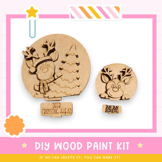 a DIY wood paint kit for creating wooden decorations, including two wooden reindeer figures. The kit appears to be designed for children, as indicated by the text "DEER CROSSING AHEAD" and "RUN RUN RUDolph". The kit is presented in a pink and white color scheme, with a star decoration on the left side. The image does not contain any text that can be described in more detail, and it does not include any additional information about the kit's contents or instructions.