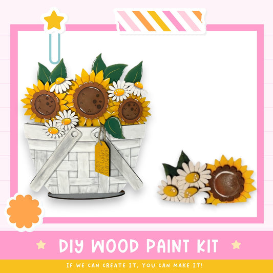 a DIY wood paint kit for creating a wooden basket with a floral design. The kit includes a white basket with a handle and a small wooden flower attached to it. The basket is filled with yellow sunflowers and white daisies. The kit is presented in a pink and white frame, and the text "DIY WOOD PAINT KIT" is displayed at the bottom.