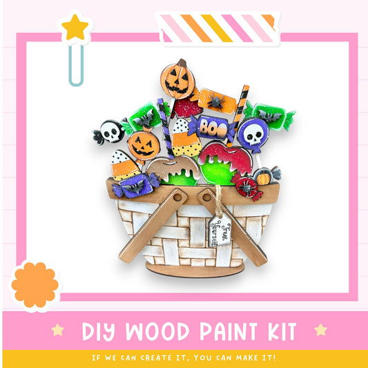 The image is a colorful and festive DIY wood paint kit, featuring a basket filled with various Halloween-themed decorations such as candy canes, bats, skulls, and pumpkins. The kit appears to be made of wood and is designed for creating custom Halloween decorations.