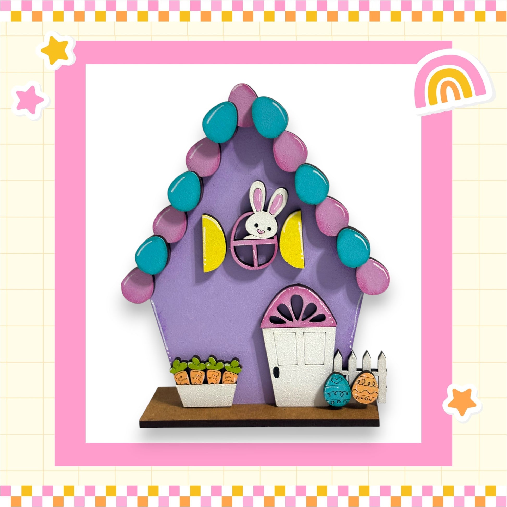 A colorful Easter-themed house made of various craft materials, including a purple and pink structure, a yellow door, and a white door. The house is decorated with Easter eggs and carrots, and there are small Easter eggs and carrots placed on the ground in front of the house.