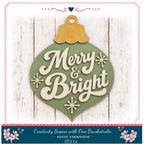 A green ornament with the text "Merry & Bright" and snowflake decorations, placed on a white wooden background.