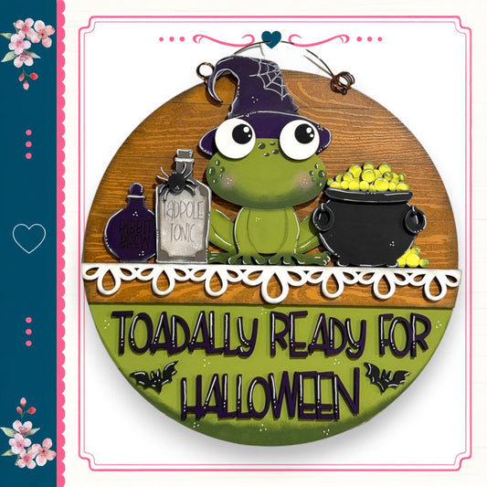 A green frog wearing a witch's hat and holding a cauldron of yellow candies, with the text "TOADALLY READY FOR HALLOWEEN" displayed below.