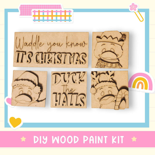 The image is a DIY wood paint kit featuring a collection of wooden shapes and characters, including a duck, a Santa Claus hat, and a rainbow.