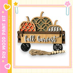 A wooden wagon with carved pumpkins and a sign that says "fall harvest" is displayed against a pink and yellow background.